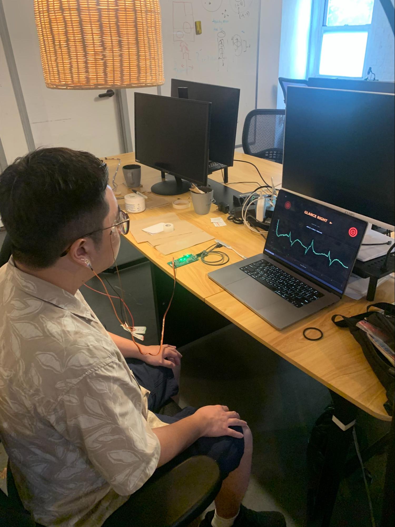 A wired-up subject sits at a laptop that prompts GLANCE RIGHT while his EOG trace scrolls across the screen.
